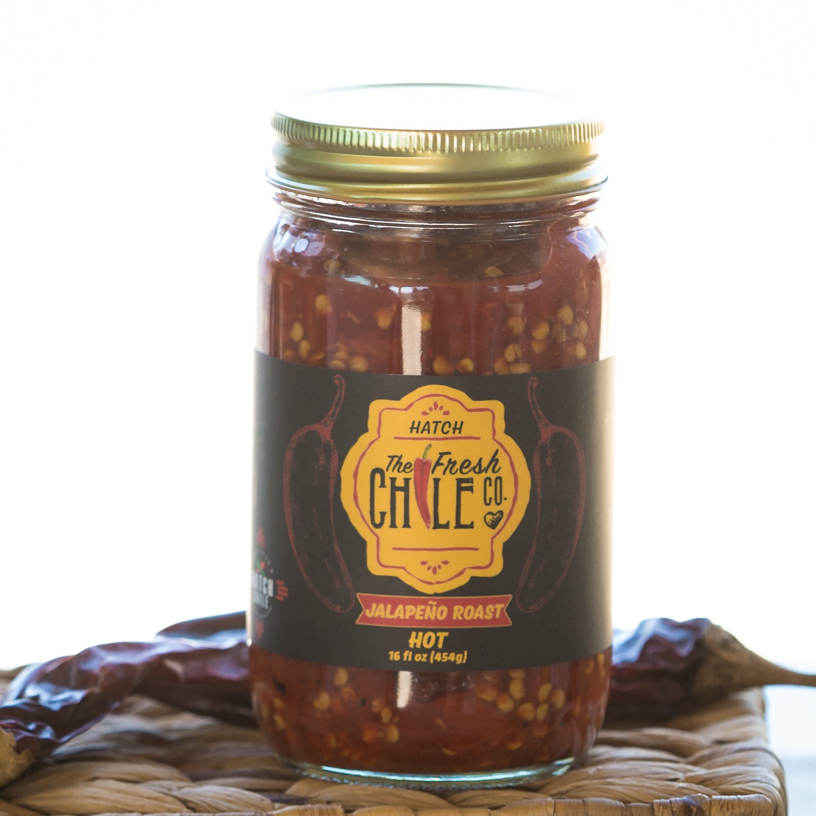 A jar of Hatch Red Jalapeño Roast hot sauce on a woven mat, prominently displayed with a label featuring red jalapeños and descriptive text.
